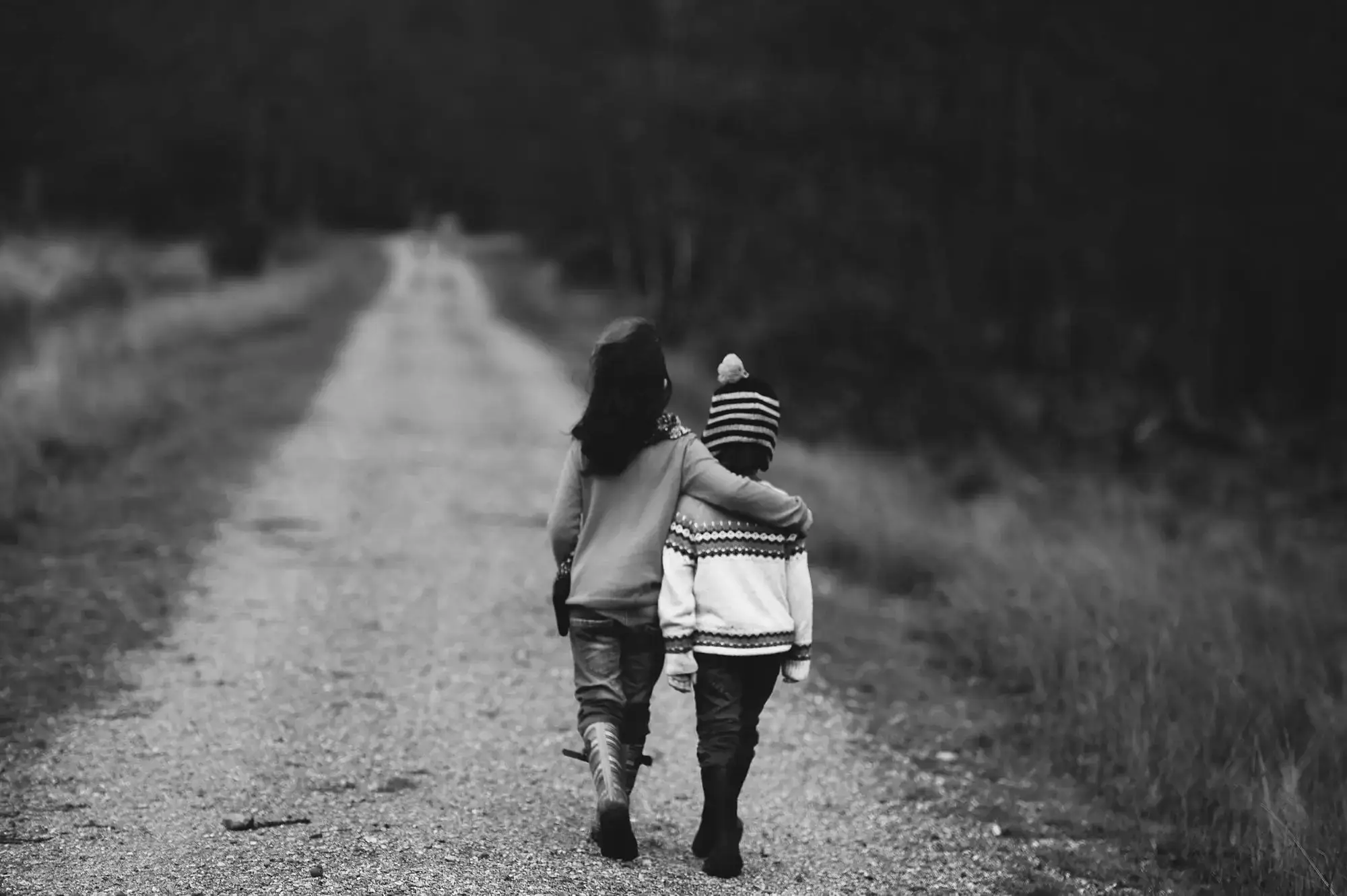 Two children walking arm-in-arm on a quiet gravel path
